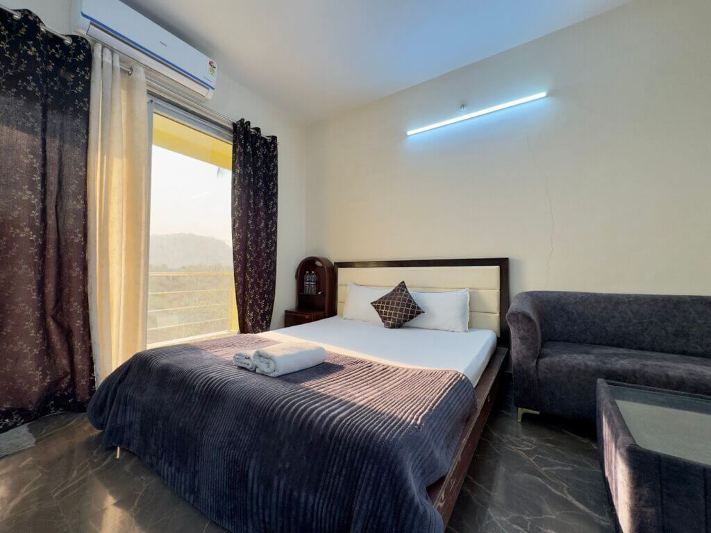 A Deluxe Room with a bed, seating and balcony doors at NB Nature Stay